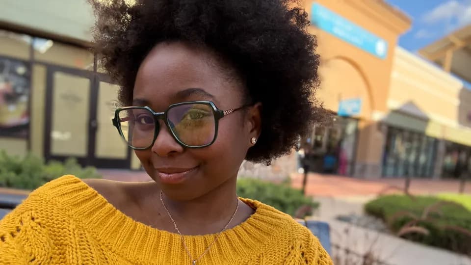 McKenzie wearing glasses and a yellow sweater outside.